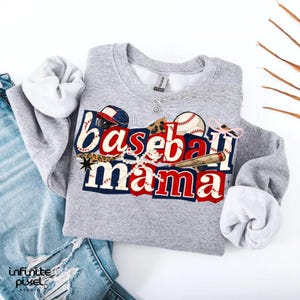 May include: A gray sweatshirt with the words "Baseball Mama" in a red, white, and blue design. The design includes baseballs, a baseball bat, and a baseball cap. The sweatshirt is paired with blue jeans.
