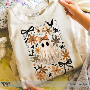 May include: Cream-coloured sweatshirt with a Halloween design. The design features a ghost with a bow, flowers, spiders, and bats. The words "digital download" are visible in the bottom right corner.