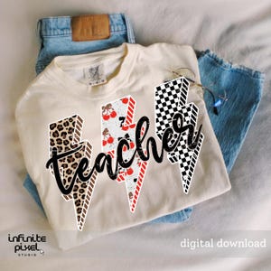 May include: Cream-colored t-shirt with the word "teacher" in black script, overlaid on three lightning bolt designs. The lightning bolts feature leopard print, cherries, and a black and white checkerboard pattern. The shirt is paired with blue jeans.