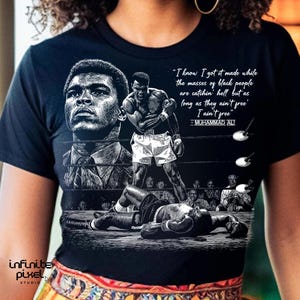 May include: Black t-shirt featuring a graphic of Muhammad Ali in a boxing ring. The design includes a portrait of Ali, a boxing match scene, and a quote: "I know I got it made while the masses of black people are catchin' hell but as long as they ain't free I ain't free."