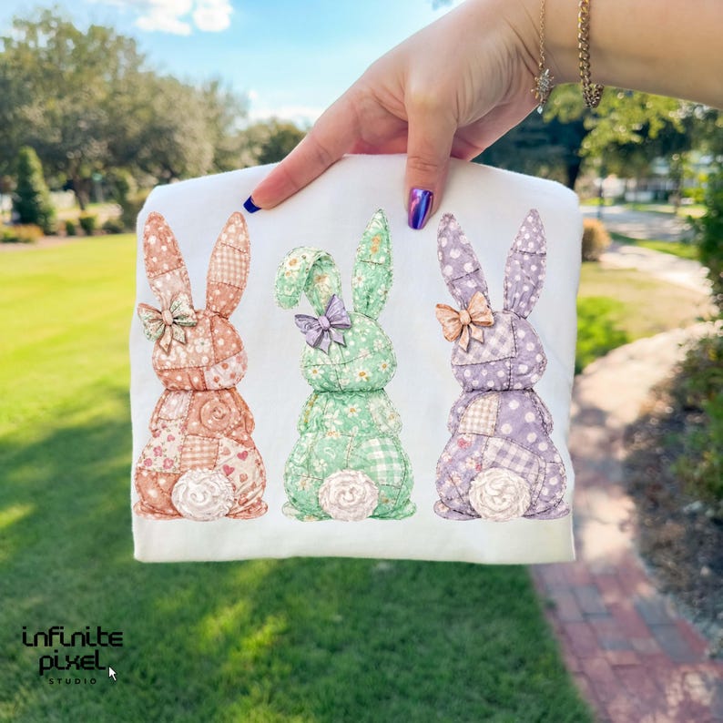 May include: White fabric featuring three patchwork bunny designs in peach, green, and purple. Each bunny has a bow and a fluffy tail. The bunnies are made of various floral and patterned fabrics. The image has the text "infinite pixel studio".