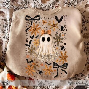 May include: Beige sweatshirt with a Halloween-themed design. The design features a ghost with an orange bow, flowers, bats, spiders, and black bows. The words "infinite pixel" and "digital download" are visible.