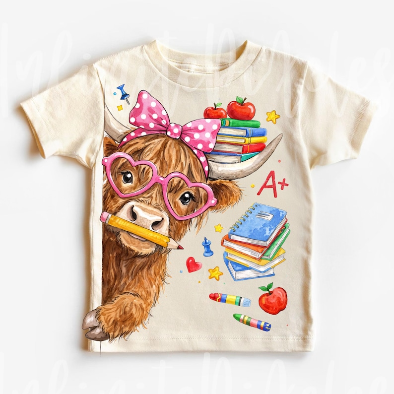 Pu&ograve; includere: T-shirt color crema con un cartone animato di una mucca delle Highlands con occhiali a forma di cuore e un fiocco a pois. La mucca tiene una matita ed &egrave; circondata da libri, mele e pastelli. La maglietta ha la scritta "A+".