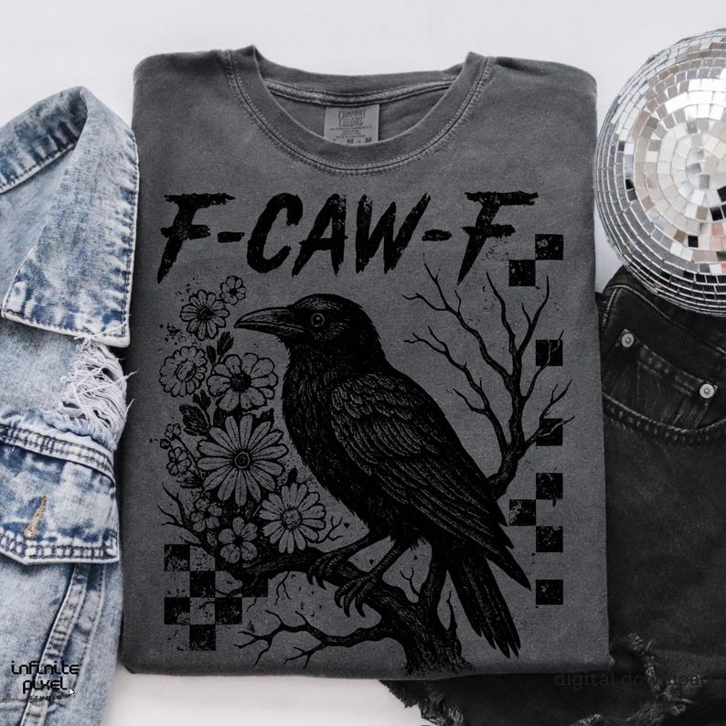 Puede incluir: Camiseta gris oscuro con un dise&ntilde;o negro de un cuervo posado en una rama, rodeado de flores y el texto "F-CAW-F". El dise&ntilde;o incluye un patr&oacute;n de cuadros y ramas de &aacute;rboles desnudas.