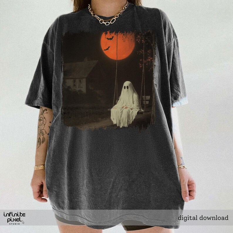 May include: Dark gray t-shirt featuring a spooky Halloween design. The graphic depicts a ghost on a swing set under a large orange moon with bats. The text "digital download" is visible at the bottom right.