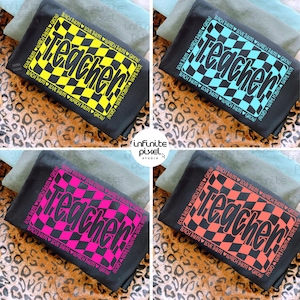 May include: Four black t-shirts with the word "Teacher" in a checkered design. The word is in yellow, blue, pink, and orange. The text "Teach them, love them, watch them grow" surrounds the checkered design.
