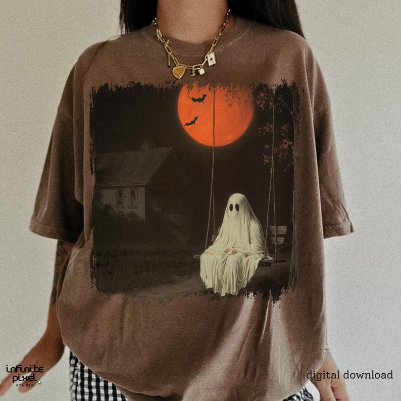 May include: Brown t-shirt featuring a spooky Halloween design. The graphic depicts a ghost on a swing set under a large orange moon, with bats flying in the sky. The text "digital download" is visible on the bottom right.
