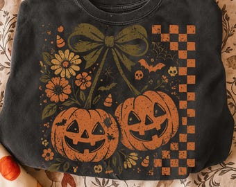 May include: Dark gray sweatshirt featuring a Halloween-themed design. The graphic includes two orange jack-o'-lanterns, a large green bow, flowers, bats, and a checkered pattern. The design has a vintage, distressed look.