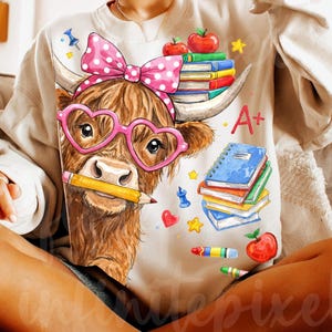 Pu&ograve; includere: Una felpa beige con un cartone animato di una mucca delle Highlands con occhiali rosa a forma di cuore e un fiocco a pois. La mucca tiene in bocca una matita, con libri, mele e la lettera "A+" stampata. Un divertente tema di ritorno a scuola.