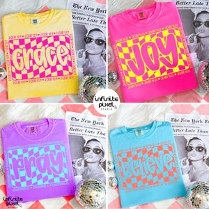 May include: Four colorful t-shirts with the words "Grace", "Joy", "Pray", and "Believe" in a retro font and checkered pattern. Each shirt has a different color: yellow, pink, purple, and blue. The shirts are displayed with a newspaper and disco ball.