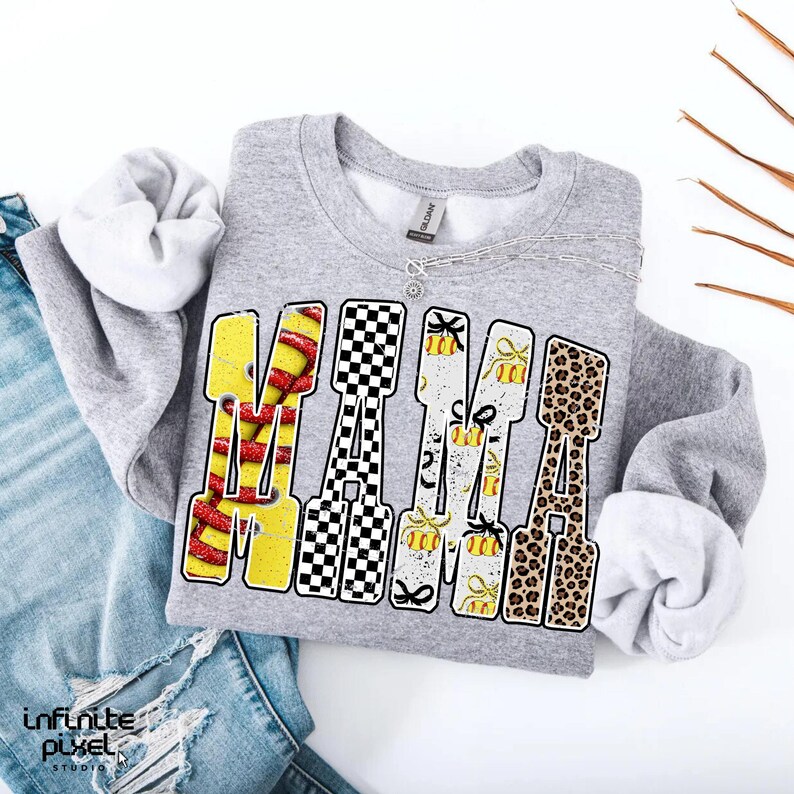 May include: A gray sweatshirt with the word "MAMA" in a bold, colorful design. The letters feature various patterns, including a red and yellow design, a black and white checkerboard, and a leopard print. A silver necklace is visible.