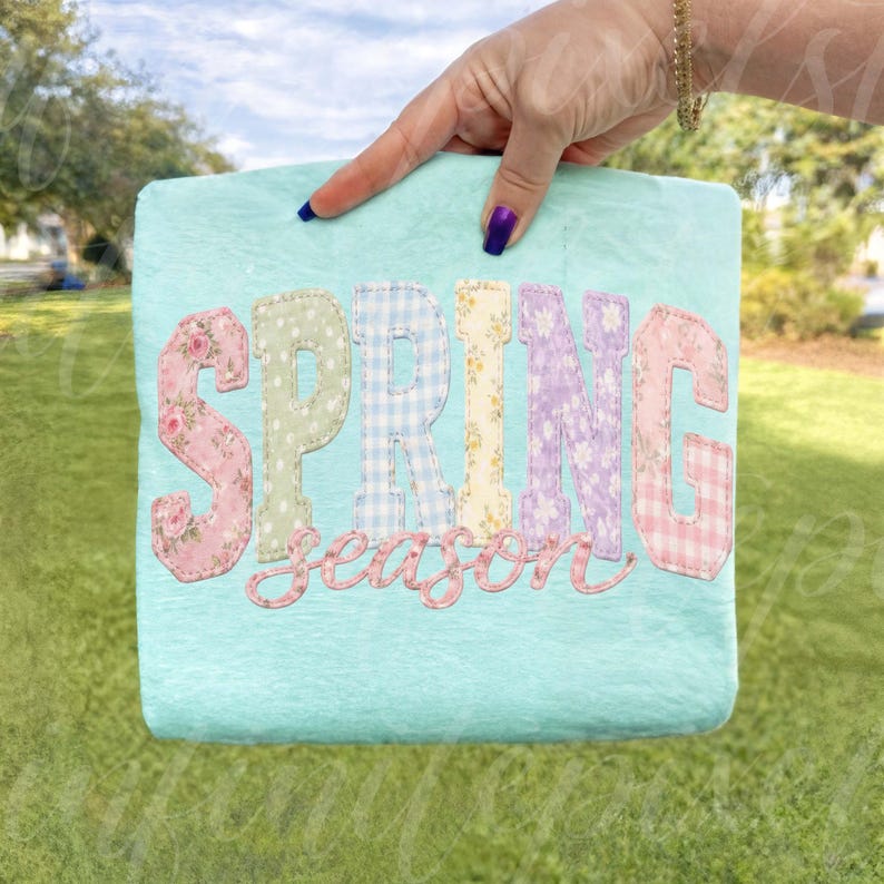 May include: A light blue square-shaped decorative item with the words "SPRING season" in colorful, patterned letters. The letters are in pink floral, green polka dot, blue gingham, yellow floral, purple floral, and pink gingham patterns.