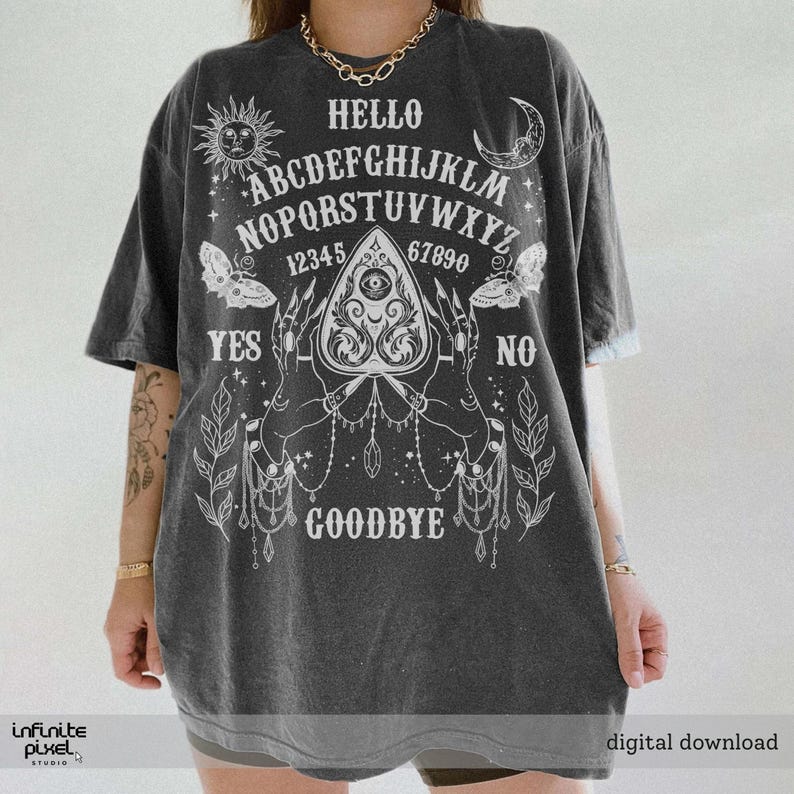 May include: Charcoal grey t-shirt featuring a white Ouija board graphic. The design includes the alphabet, numbers, sun, moon, butterflies, and the words "Hello", "Yes", "No", and "Goodbye".
