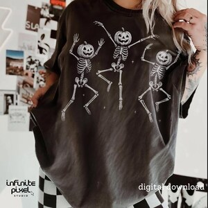 May include: Dark gray t-shirt featuring three dancing skeletons with pumpkin heads. The skeletons are white and have their arms and legs outstretched. The words "digital download" are printed on the bottom right.