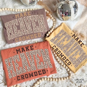 May include: Three t-shirts in shades of brown, orange, and yellow, each with the text "MAKE HEAVEN CROWDED" in a leopard print design. The shirts are arranged on a white surface with decorative beads and disco balls.