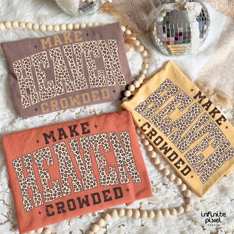 May include: Three t-shirts in shades of brown, orange, and yellow, each with the text "MAKE HEAVEN CROWDED" in a leopard print design. The shirts are arranged on a white surface with decorative beads and disco balls.