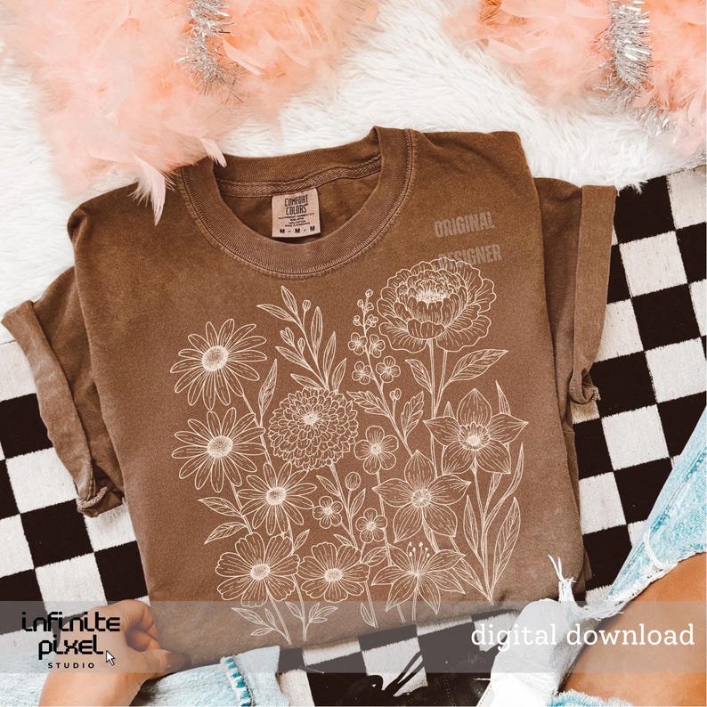 May include: A brown t-shirt featuring a white floral design. The shirt has short sleeves and a crew neck. The words "ORIGINAL DESIGNER" are printed on the upper right side. The words "digital download" are printed on the bottom right side.
