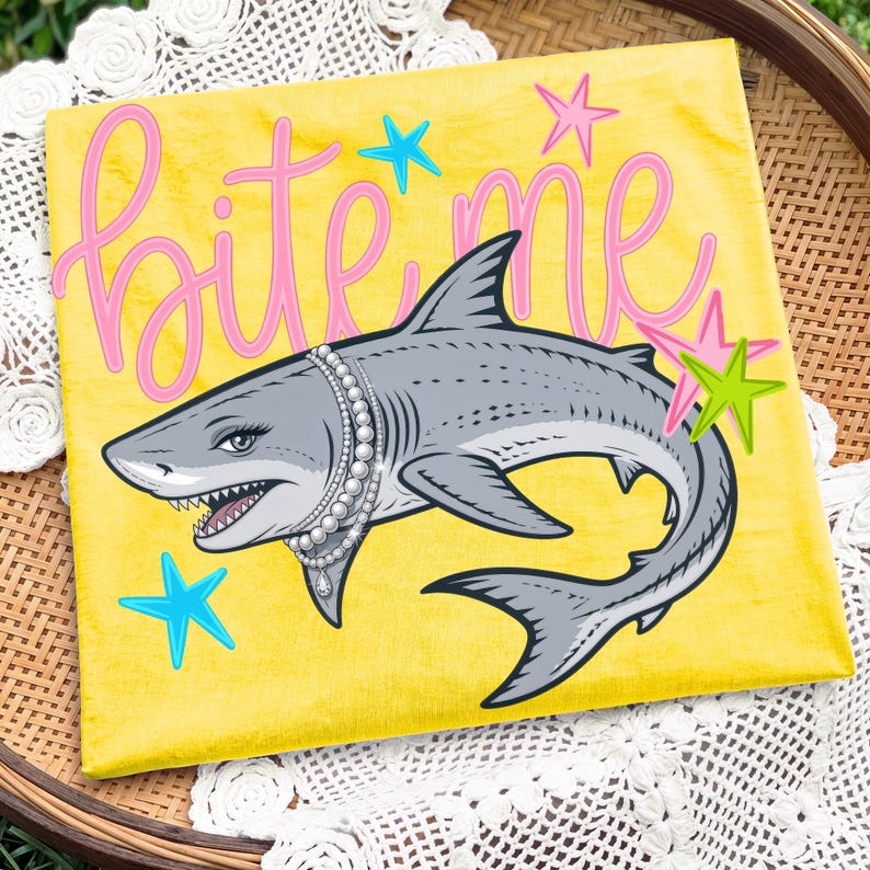 May include: A yellow canvas with a cartoon shark wearing a pearl necklace. The shark has a sassy expression and the words "Bite Me" in pink script. Blue, pink, and green starfish are scattered around the shark.
