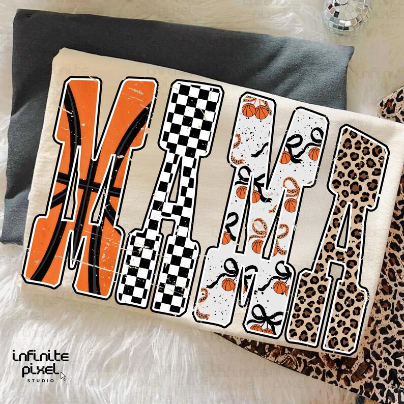Puede incluir: Una camiseta color crema con la palabra "MAMA" en letras grandes y en negrita. Cada letra tiene un dise&ntilde;o &uacute;nico: baloncesto, a cuadros, estampado de baloncesto y serpiente, y estampado de leopardo. La camiseta est&aacute; doblada sobre una superficie gris.