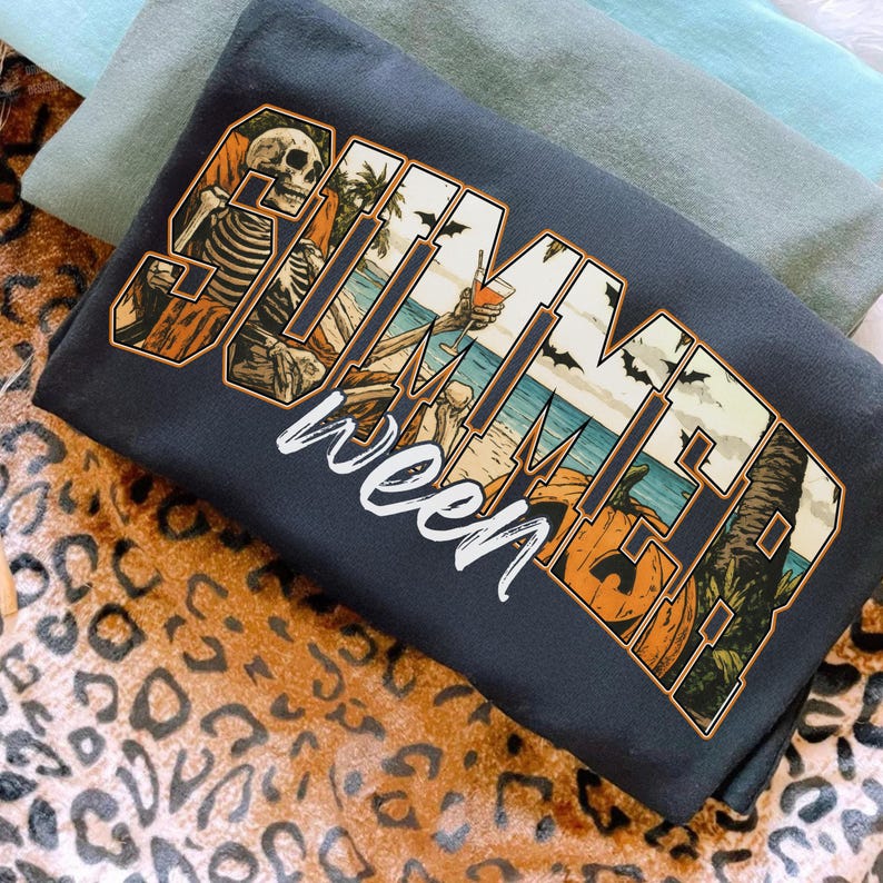 May include: Dark gray t-shirt with the words "Summerween" in a stylized design. The design incorporates a skeleton, beach scene, bats, and pumpkins, blending summer and Halloween themes.