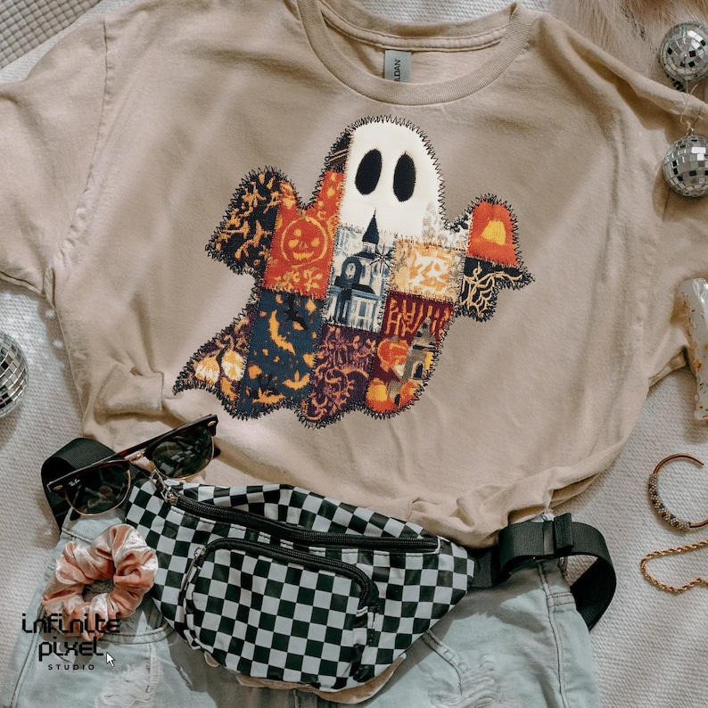 Puede incluir: Una camiseta beige con un dise&ntilde;o de fantasma de patchwork con patrones de Halloween. La imagen tambi&eacute;n incluye una ri&ntilde;onera a cuadros en blanco y negro, gafas de sol y una goma para el pelo. Tambi&eacute;n se ven bolas de discoteca y joyas.