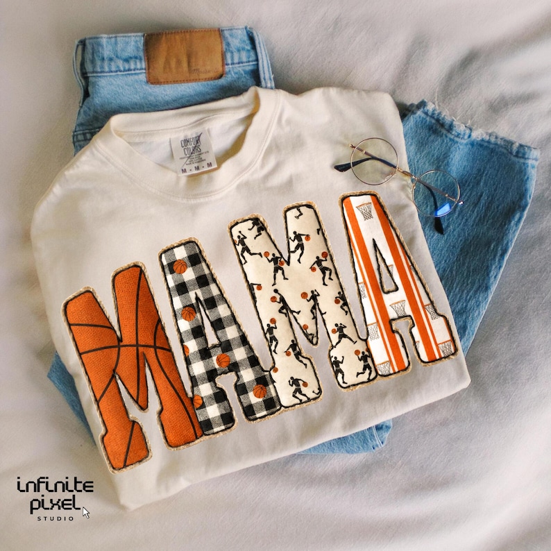 Puede incluir: Sudadera de color crema con la palabra "MAMA" en letras grandes y decorativas. La "M" es naranja con un dise&ntilde;o de baloncesto, la "A" es naranja con un dise&ntilde;o de canasta de baloncesto, y las otras letras tienen patrones de baloncesto y jugadores. La sudadera se combina con vaqueros azules y gafas.