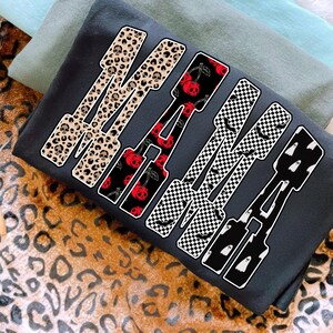 May include: Dark gray sweatshirt with the word "MAMA" in a bold, stylized font. Each letter features a unique pattern: leopard print with skulls, red cherries, black and white checkerboard with bats, and white ghosts.