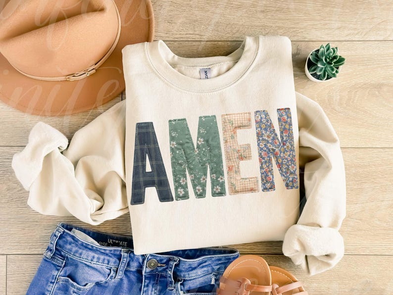 May include: Cream-colored sweatshirt with the word "AMEN" in patchwork letters. The letters are made of various patterned fabrics, including plaid, floral, and gingham. The sweatshirt is paired with blue jeans, sandals, and a hat.