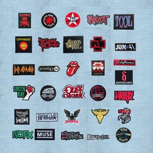 Peut inclure: Collection de patchs brodés représentant des groupes de rock et de métal, dont Red Hot Chili Peppers, The Clash et Green Day. Les patchs sont de formes et de tailles variées, avec des couleurs vives et des motifs détaillés. Ils sont présentés sur un tissu bleu clair.