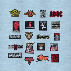 Könnte beinhalten: Eine Sammlung gestickter Aufnäher mit Logos verschiedener Rock- und Metalbands, darunter AC/DC, Misfits und System of a Down. Die Aufnäher sind in verschiedenen Farben und Formen gehalten und weisen Texte und grafische Designs auf. Sie sind auf hellblauem Stoff angeordnet.