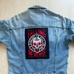 May include: Light blue denim jacket with a large black patch on the back. The patch features a skull graphic with the words "Falling Straight to Hell for Me in Reverse" in red and white.