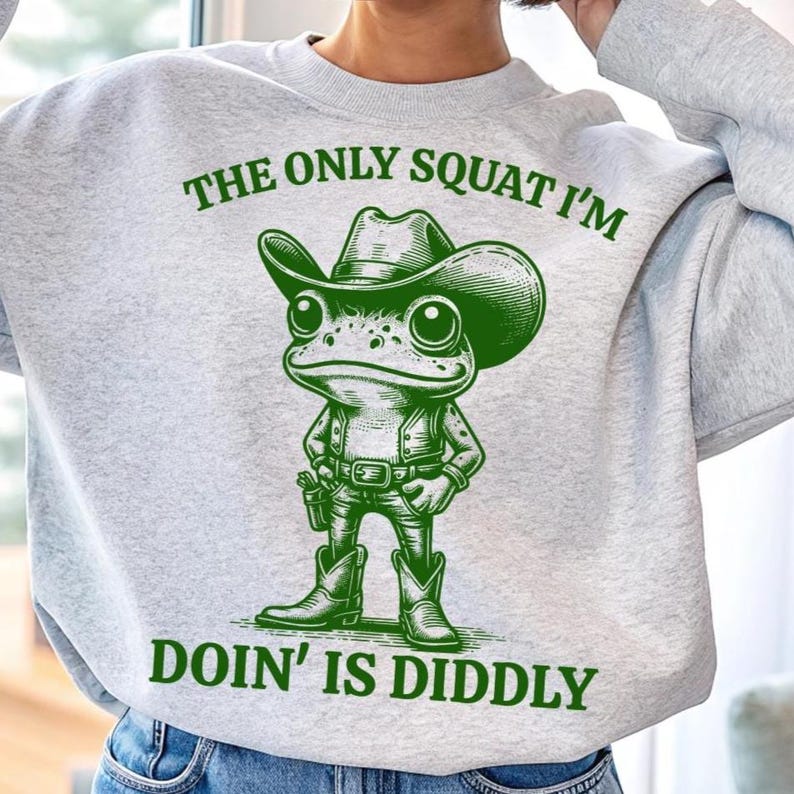 Może przedstawiać: Szara bluza z zieloną żabą w kowbojskim kapeluszu i napisem "The only squat I'm doin' is diddly".