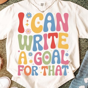 Könnte beinhalten: Cremefarbenes T-Shirt mit dem Schriftzug "I CAN WRITE A GOAL FOR THAT" in farbenfrohen Retro-Lettern. Das Design beinhaltet Blumen und Sterne. Das Shirt ist aus weichem Material.