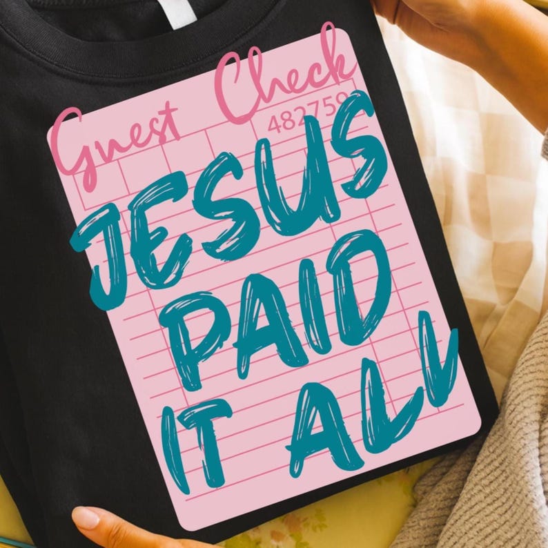 May include: Black t-shirt with a pink graphic resembling a guest check. The graphic reads "Guest Check" in pink script, with the words "JESUS PAID IT ALL" in teal, and a number "482759".