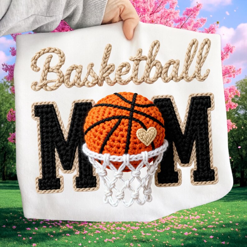 May include: White fabric with the words "Basketball MOM" in a decorative font. The word "Basketball" is in a rope-like font. The "MOM" is in a black block letter style with a rope-like border. A crocheted basketball is in the center, with a heart and net.