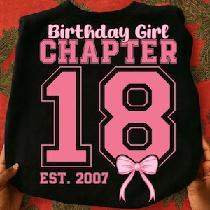 Peut inclure: Sweat-shirt noir avec texte rose "Birthday Girl CHAPTER 18 EST. 2007" et un nœud rose. Le chiffre 18 est dans une police de style universitaire. Le sweat-shirt est un col rond.