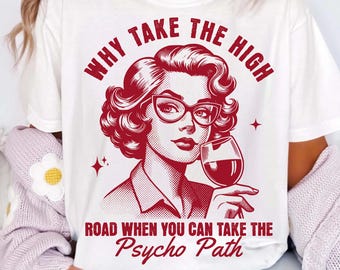 May include: White t-shirt with a red graphic of a woman wearing glasses and holding a wine glass. The text on the shirt reads "WHY TAKE THE HIGH ROAD WHEN YOU CAN TAKE THE Psycho Path."