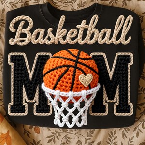 May include: Black sweatshirt with the words "Basketball Mom" in beige and black. The letter "M" is in black with a beige border. An orange and black basketball is in the center, with a white net and a beige heart.