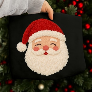 May include: Black pillow featuring a smiling Santa Claus face. The Santa has a red hat with white trim, a fluffy white beard, rosy cheeks, and a red mouth. The pillow is held by a person.