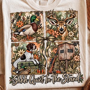 Puede incluir: Una camiseta color crema con un gráfico de cuatro paneles que muestra un pato real, una cabeza de ciervo, un perro de caza moteado y un puesto de caza con un rifle. Un lazo central une los paneles, con el texto Shhhh Quiet In The Stand.