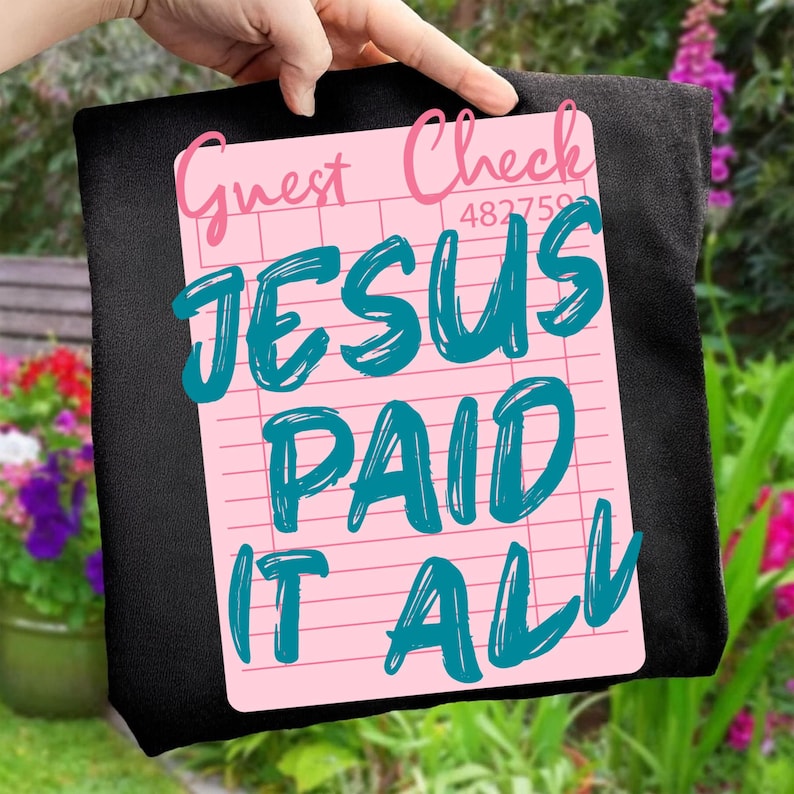 May include: A black tote bag with a pink guest check design. The guest check has the words "Guest Check" in pink script, and the words "JESUS PAID IT ALL" in teal script.