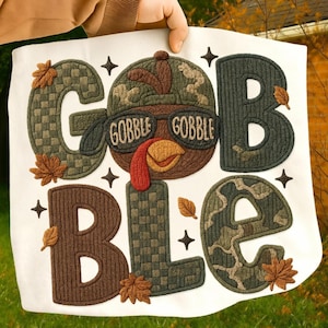 May include: A white fabric square with the word "GOBBLE" in large, textured letters. The "O" is a turkey wearing sunglasses that say "GOBBLE GOBBLE." Brown and green colors are used throughout, with fall leaves and star accents.