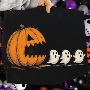 May include: Black Halloween-themed graphic featuring an orange jack-o'-lantern with a jagged mouth and three white ghosts that say "Boo". The design is on a black background.