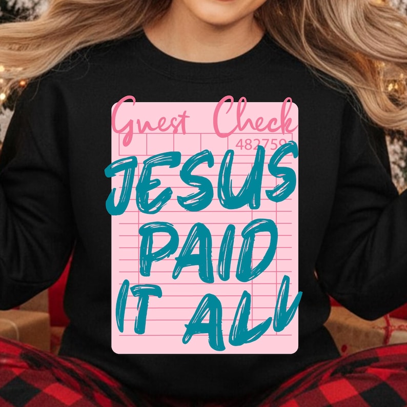 May include: Black sweatshirt featuring a pink guest check design with the words "Guest Check" and "JESUS PAID IT ALL" in teal. The design includes a check number. A cozy and inspirational apparel item.