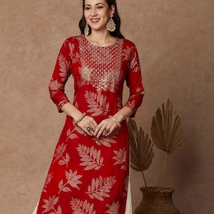 May include: A red and gold kurta with a leaf print and a white layered skirt. The kurta has a round neckline and three-quarter sleeves. The skirt has a gold trim.
