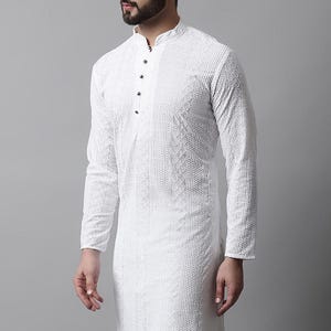 May include: White long-sleeved tunic with a mandarin collar and a textured, patterned design. The tunic has a button-down front and a tailored fit. The garment is part of a traditional South Asian clothing collection.