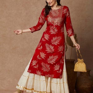 May include: A red and gold kurta with a leaf print and a white layered skirt. The kurta has a round neckline and three-quarter sleeves. The skirt has a gold trim.