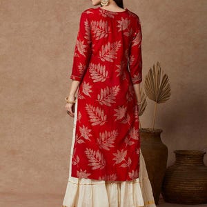 May include: A red long-sleeved kurta with a gold leaf print and a white skirt with gold trim. The kurta has a round neckline and three-quarter sleeves.