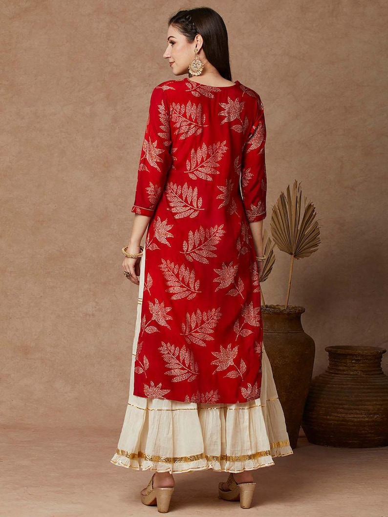 May include: A red long-sleeved kurta with a gold leaf print and a white skirt with gold trim. The kurta has a round neckline and three-quarter sleeves.