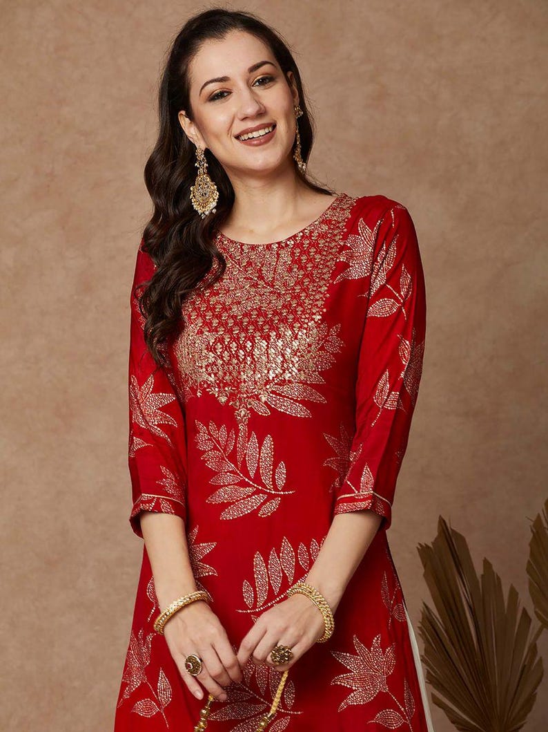 May include: A red kurta with a gold leaf print and gold embroidery. The kurta has a round neckline and three-quarter sleeves.